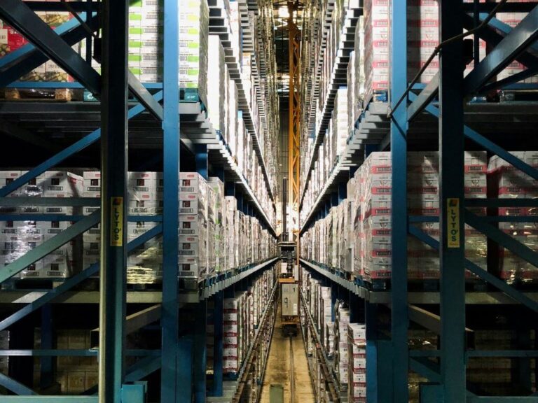 Warehouse aisle filled with stacked pallets of FMCG products on high shelves.